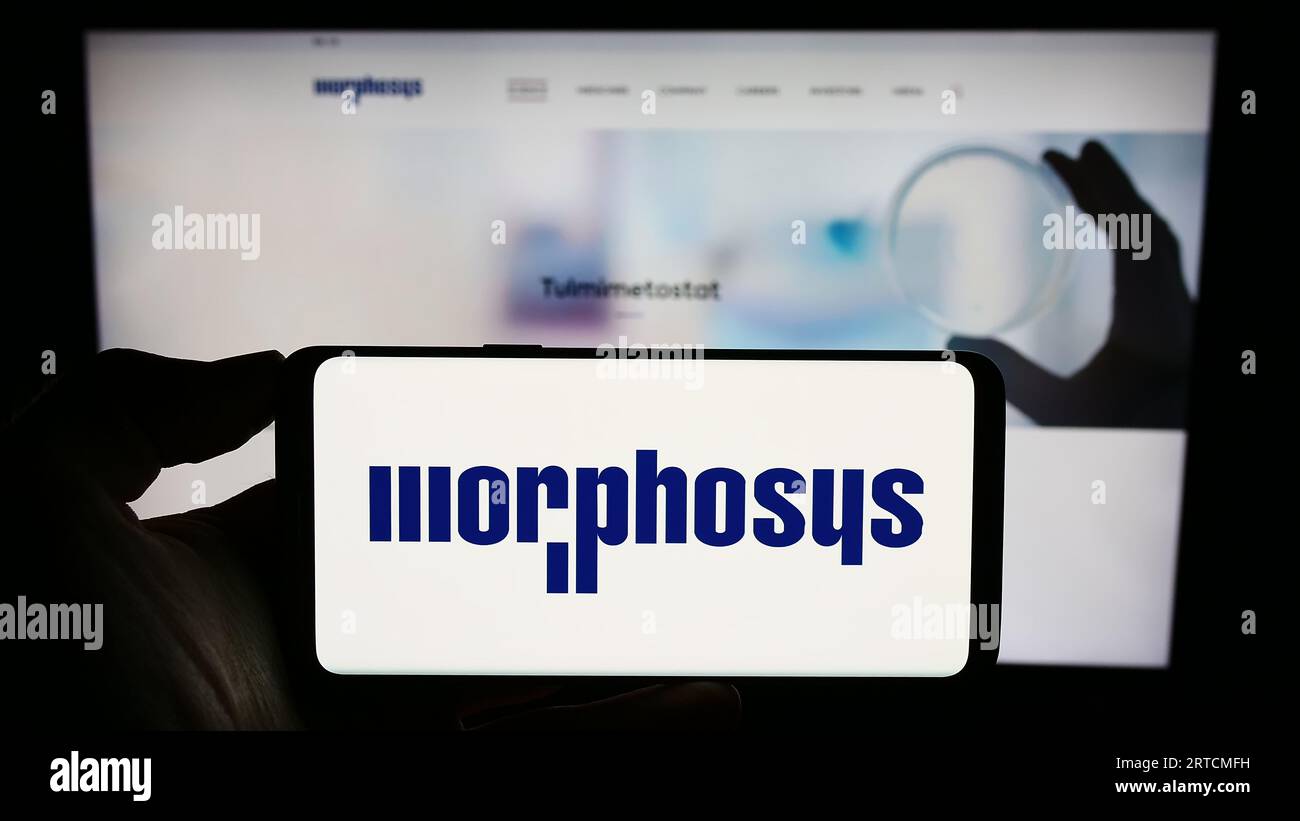 Persona che possiede uno smartphone con il logo dell'azienda biofarmaceutica tedesca MorphoSys AG sullo schermo davanti al sito Web. Concentrarsi sul display del telefono. Foto Stock