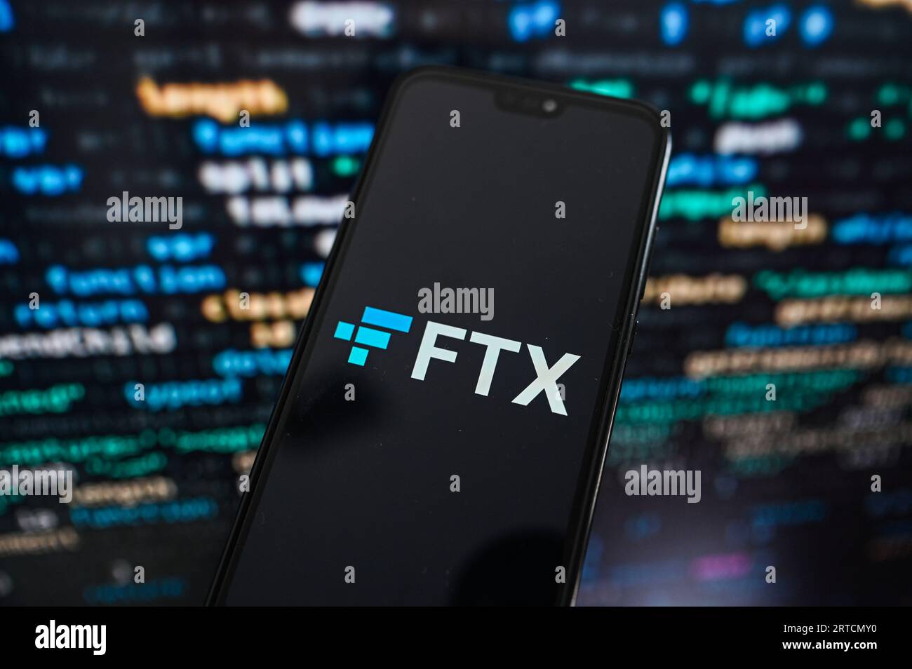 In questa foto, un logo FTX viene visualizzato su uno smartphone con il codice di programmazione sullo sfondo. Foto Stock