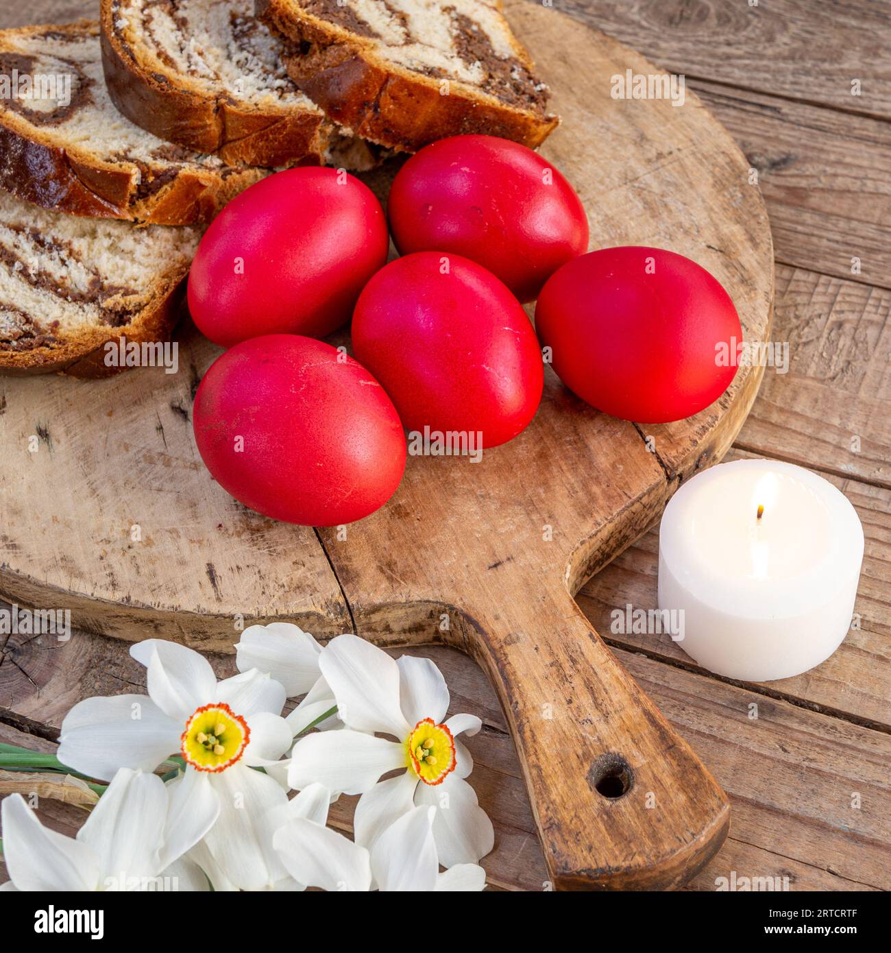 Tradizionale piatto pasquale rumeno, cozonac o pane dolce su tavola di legno, uova di pasqua colorate e fiori bianchi di narciso Foto Stock