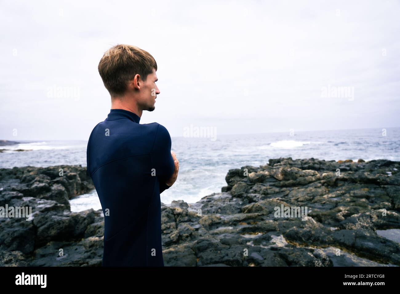 buon surfista, con i capelli biondi, guardando le onde prima di andare al surf in una giornata nuvolosa Foto Stock