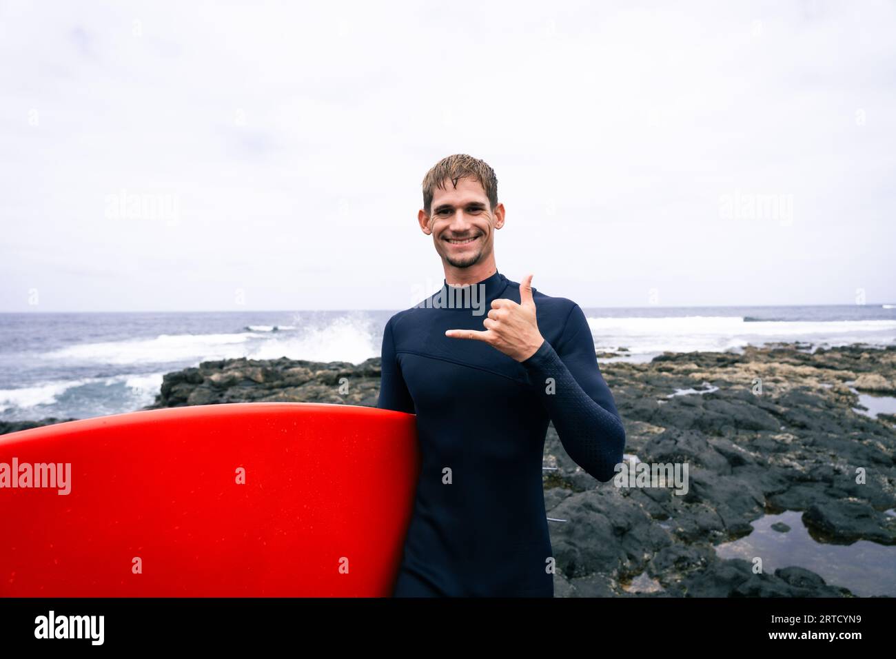 buon surfista, con i capelli biondi, guardando le onde prima di andare al surf in una giornata nuvolosa Foto Stock