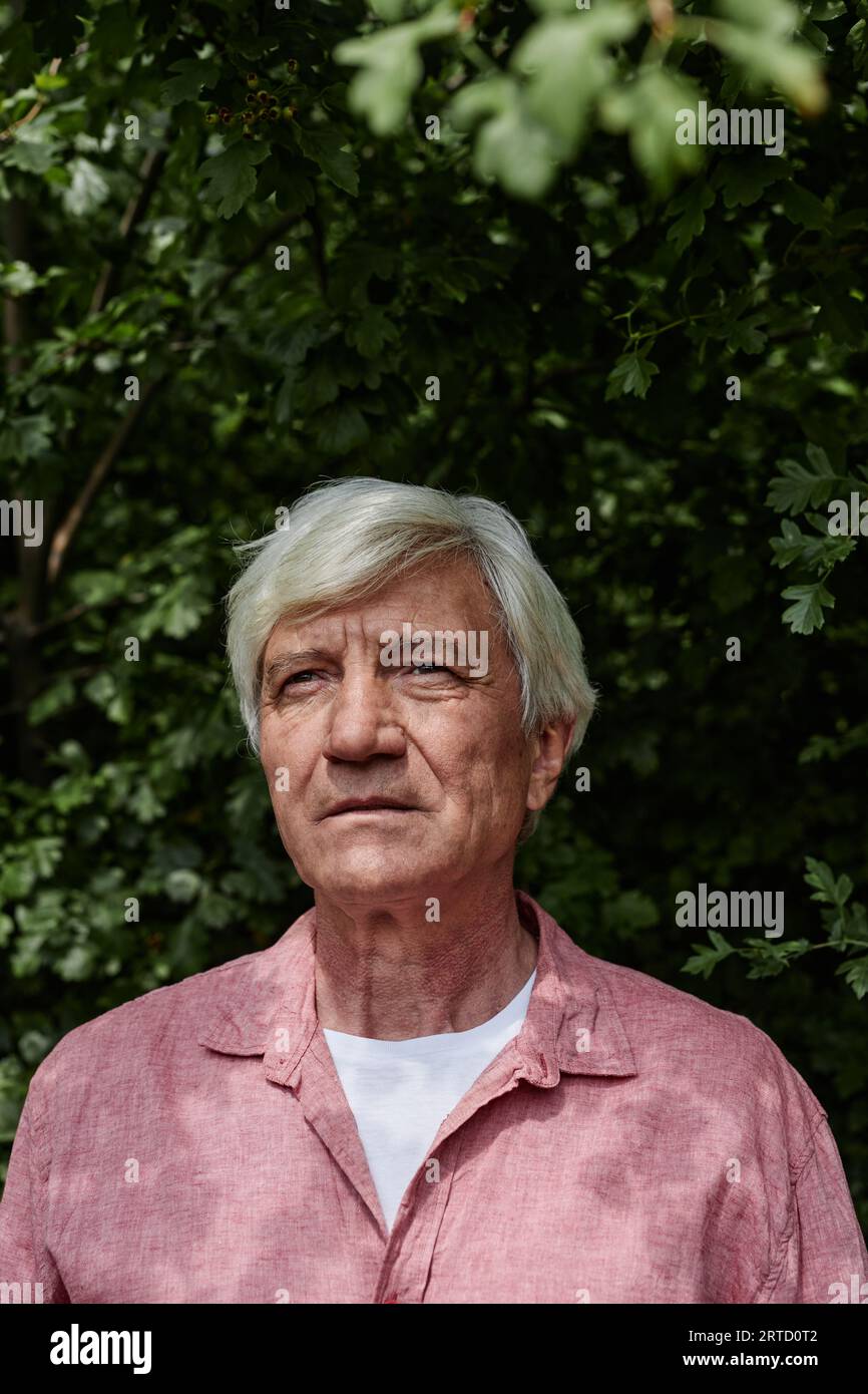 Ritratto frontale di un uomo anziano dai capelli bianchi in piedi contro il verde all'aperto Foto Stock
