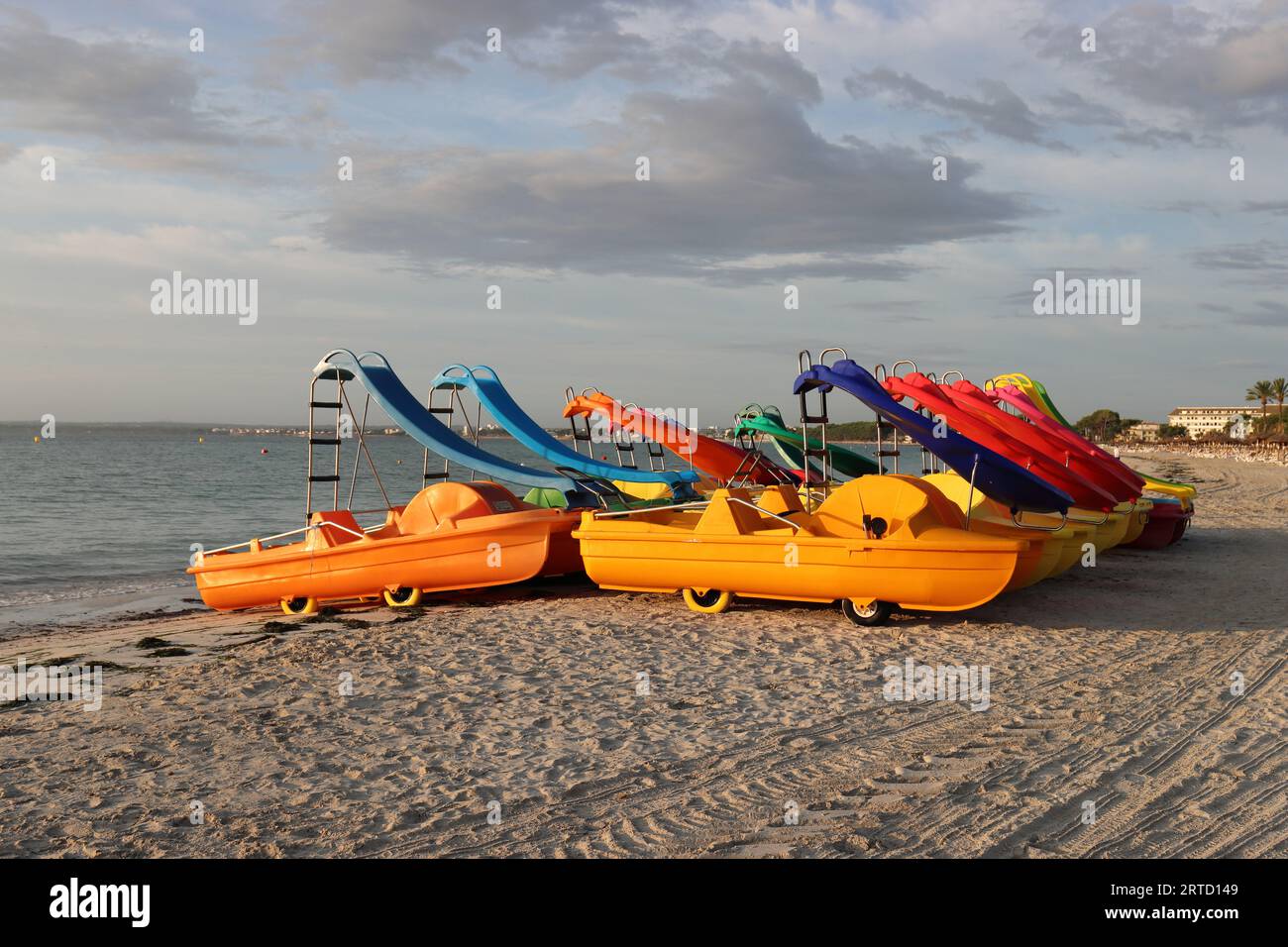 Vista delle graziose pedalò colorate sulla spiaggia sabbiosa di Alcudia illuminata dal sole mattutino Foto Stock