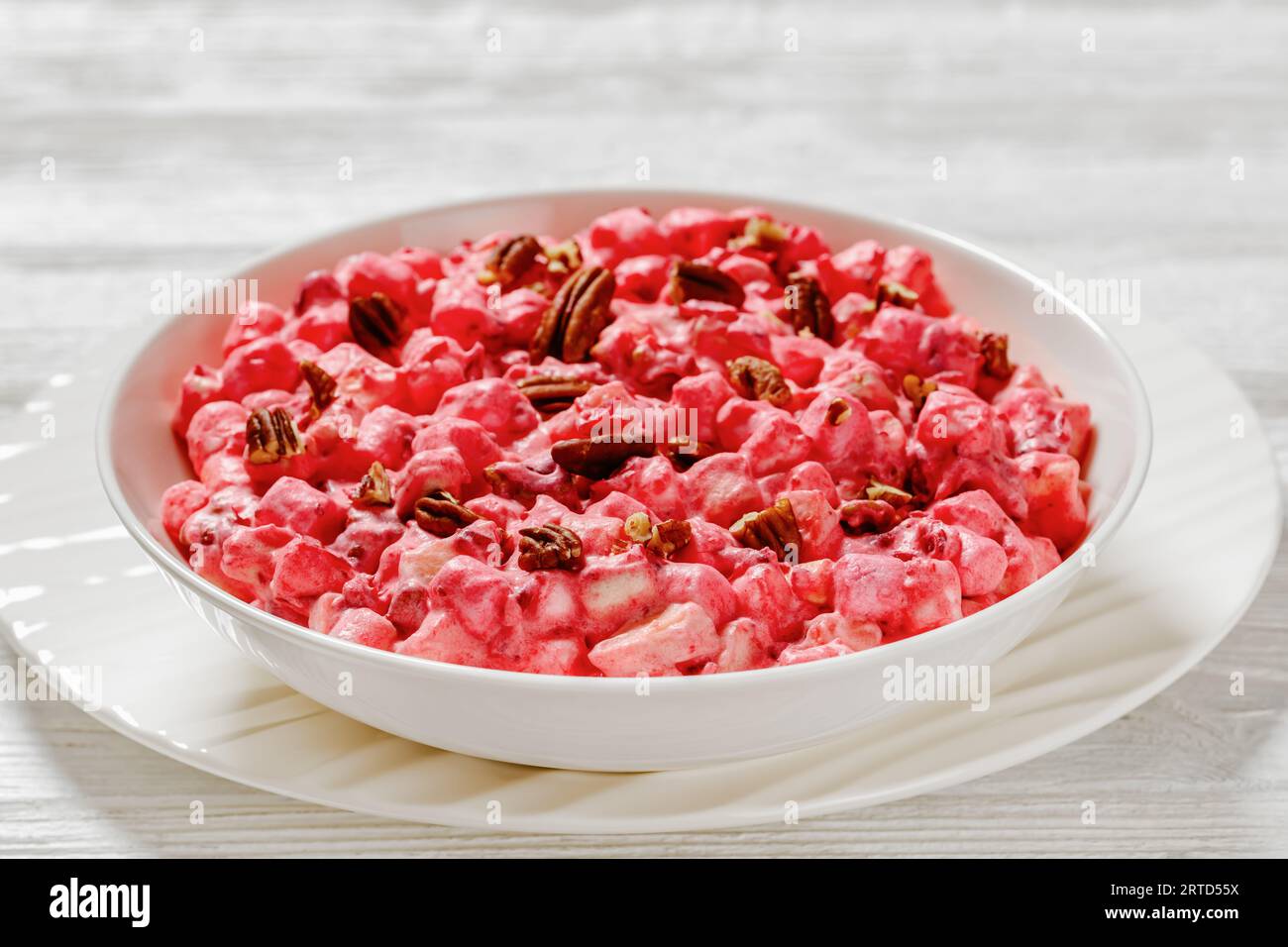 insalata cremosa di mirtilli rossi con mini marshmallow, mela fresca e noci pecan in una ciotola bianca su un tavolo di legno bianco Foto Stock