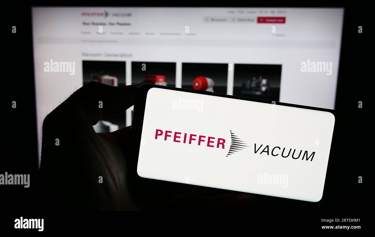 Persona che possiede uno smartphone con il logo della società tedesca Pfeiffer Vacuum Technology AG sullo schermo davanti al sito Web. Concentrarsi sul display del telefono. Foto Stock