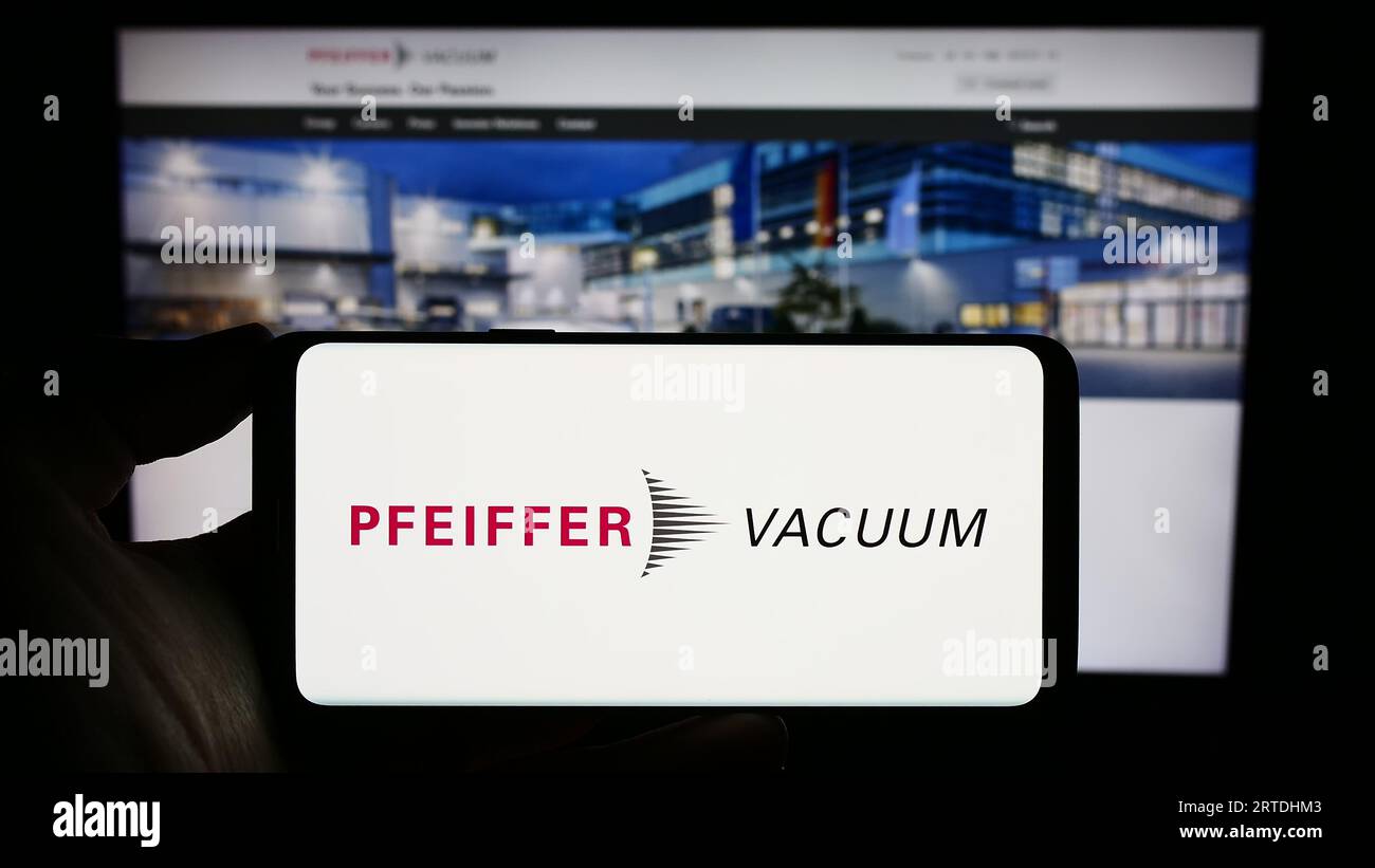 Persona che tiene il cellulare con il logo della società tedesca Pfeiffer Vacuum Technology AG sullo schermo davanti alla pagina Web. Concentrarsi sul display del telefono. Foto Stock