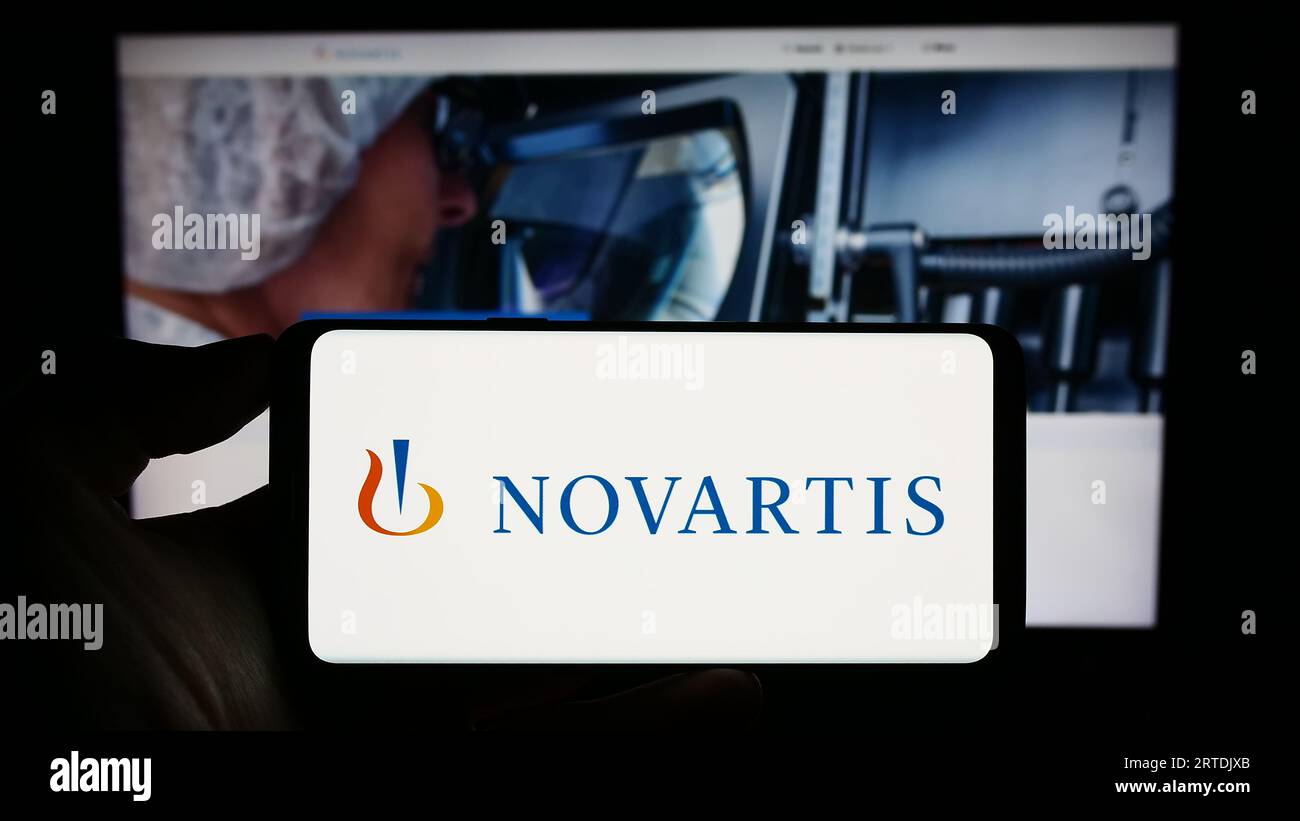Persona in possesso di un cellulare con il logo della società farmaceutica svizzera Novartis AG sullo schermo davanti alla pagina Web aziendale. Concentrarsi sul display del telefono. Foto Stock