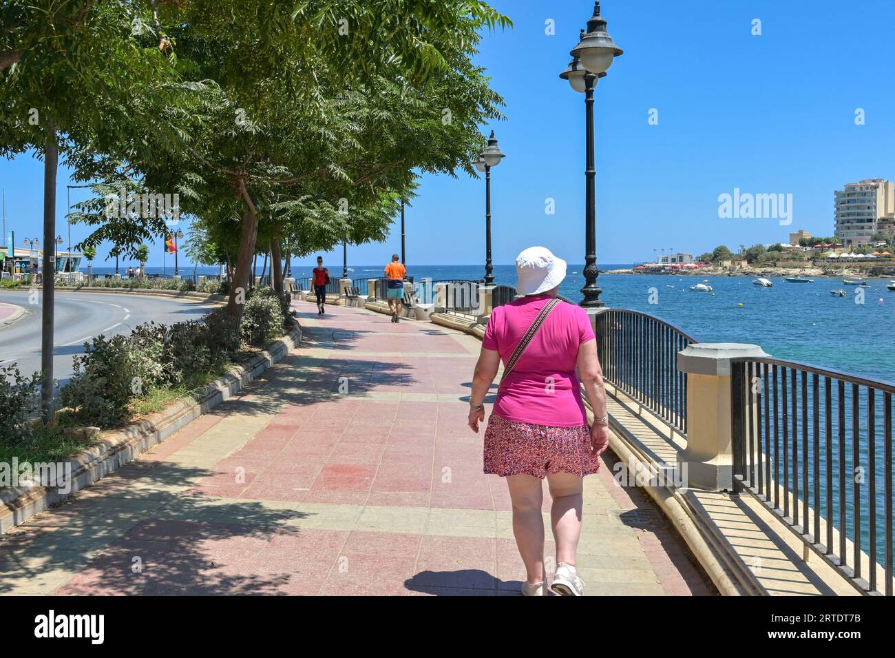 St Julians, Malta - 2 agosto 2023: Persona che cammina lungo la passeggiata intorno alla baia di St Julian Foto Stock