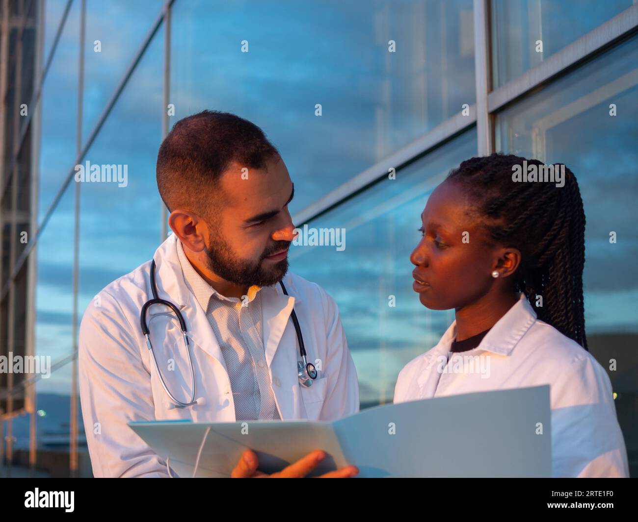 Due medici ospedalieri, una donna e un uomo, che fanno una pausa all'aperto. Guardatevi mentre sorridete. Foto Stock