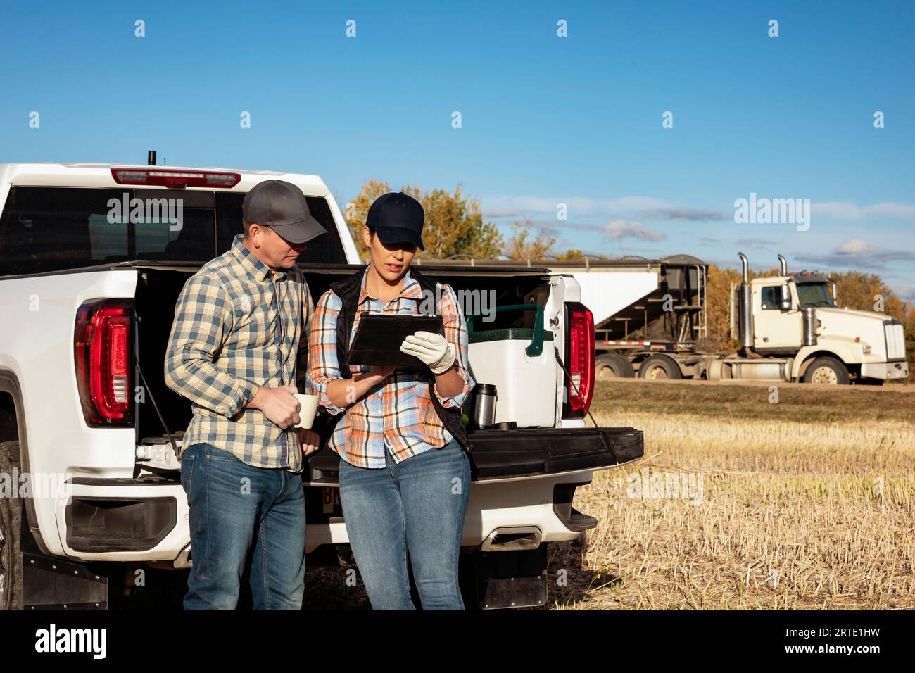 Marito e moglie si prendono del tempo per un caffè mentre si appoggiano sul portellone del loro camion da mezza tonnellata e utilizzano un dispositivo wireless portatile per la gestione e ... Foto Stock