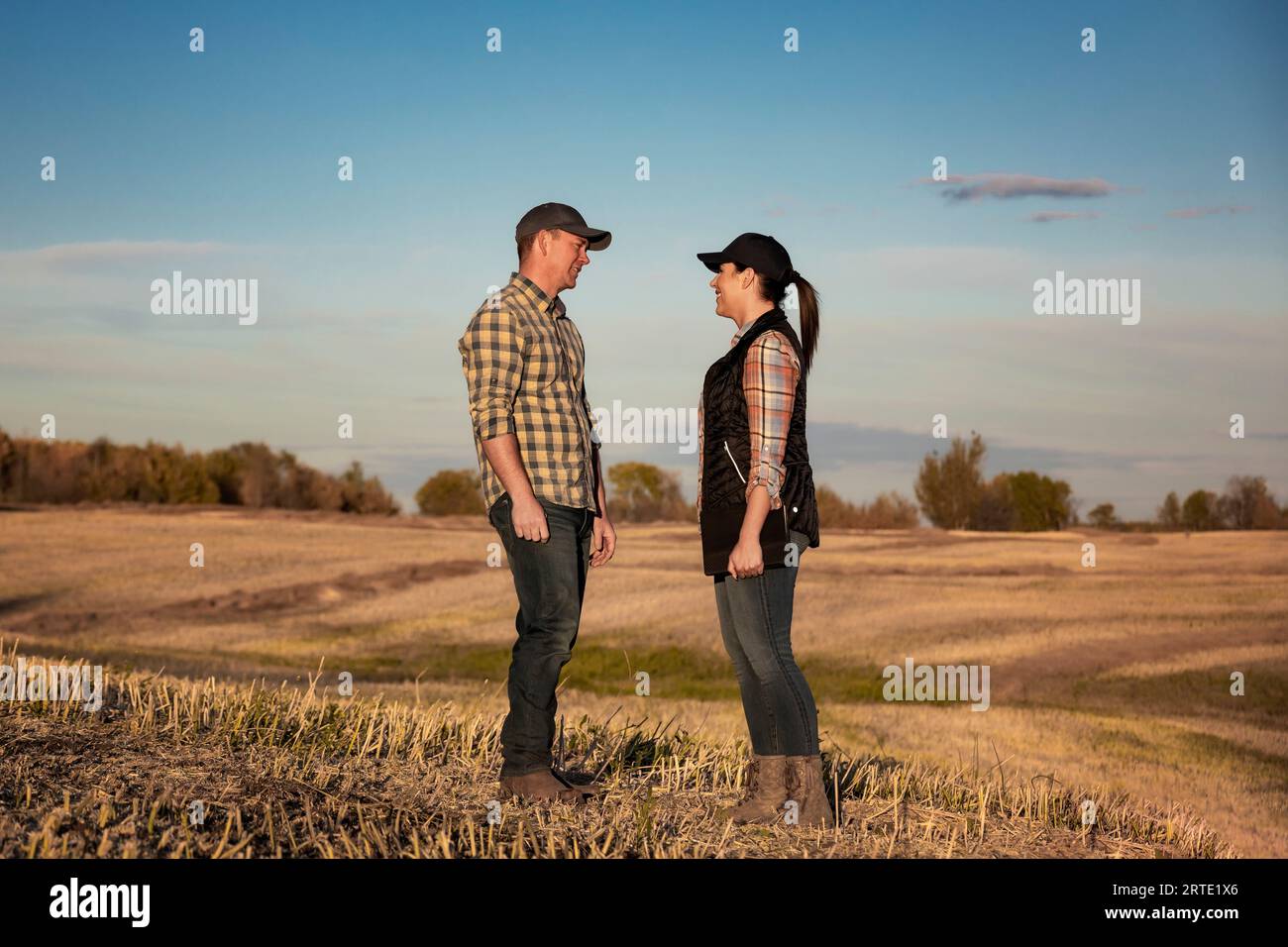 Un marito e una moglie in piedi faccia a faccia in un campo che trascorrono un po' di tempo insieme dopo aver completato il loro raccolto di canola autunnale Foto Stock