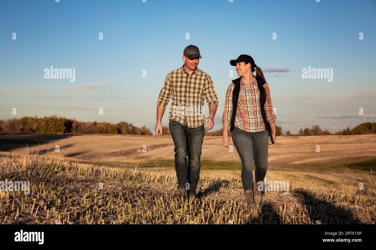 Un marito e una moglie in piedi faccia a faccia in un campo che trascorrono un po' di tempo insieme dopo aver completato il loro raccolto di canola autunnale Foto Stock