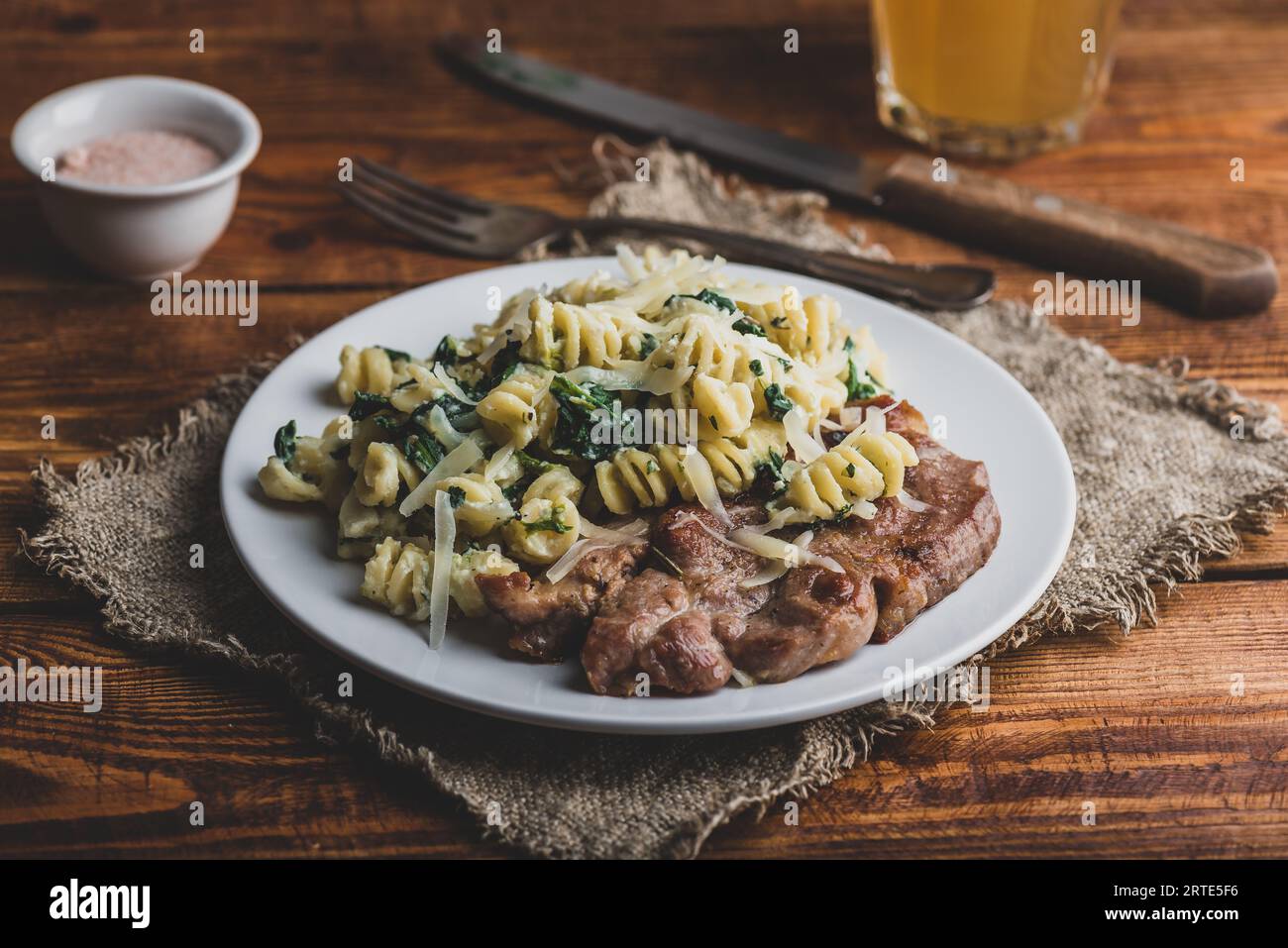 Bistecca di maiale e pasta cremosa di spinaci guarnita con parmigiano Sulla piastra bianca Foto Stock