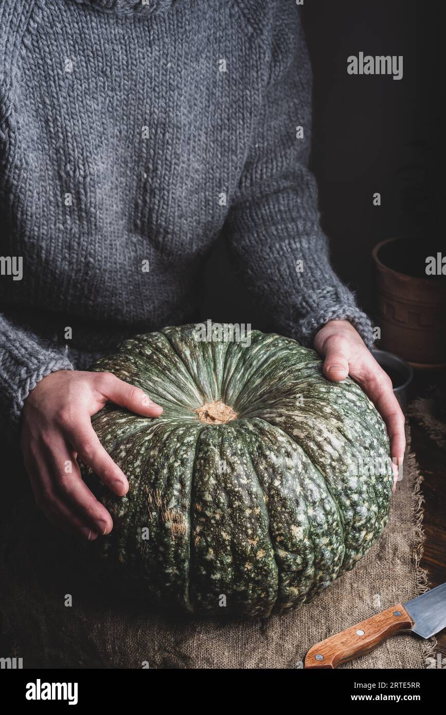 Mani maschili che mettono Big Green Pumpkin sul tavolo Foto Stock