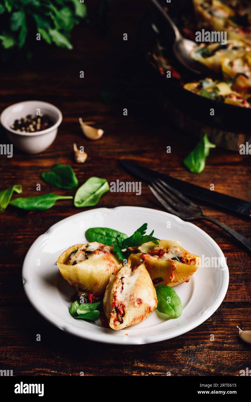 Conchiglie di jumbo al forno farcite con manzo macinato, spinaci e formaggio su piatto bianco Foto Stock