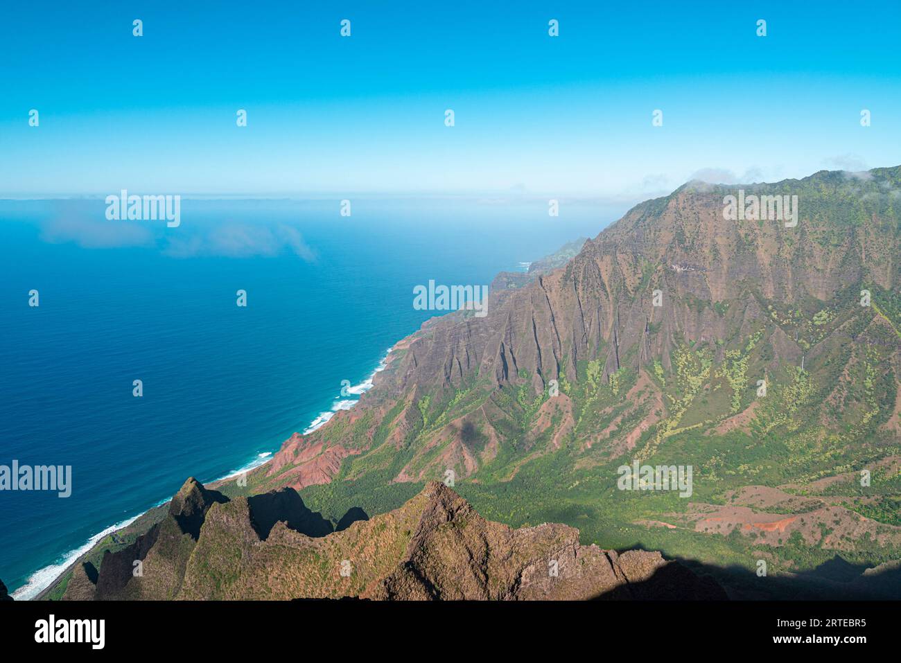 Vista panoramica delle verdi scogliere di montagna coperte della costa di Napali lungo il Kalalau Trail sull'isola hawaiana di Kauai, contro il calmo blu... Foto Stock