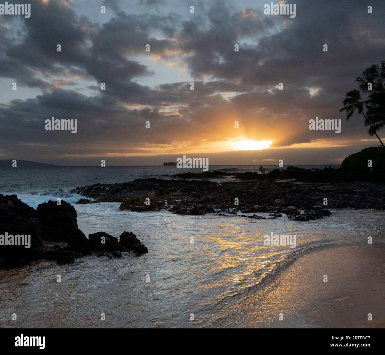 Il sole splende attraverso le nuvole e riflette sull'acqua a Secret Beach guardando la baia e l'Oceano Pacifico al crepuscolo con la silhouette o... Foto Stock