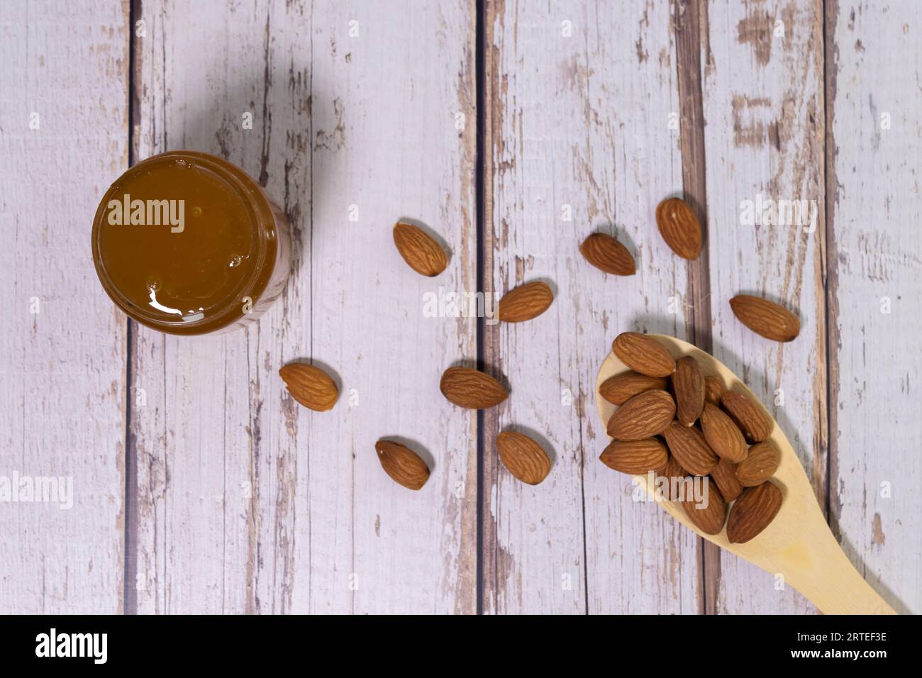 Forma di cuore fatta di più semi di mandorle accanto al legno cucchiaio di misura isolati su sfondo bianco Foto Stock