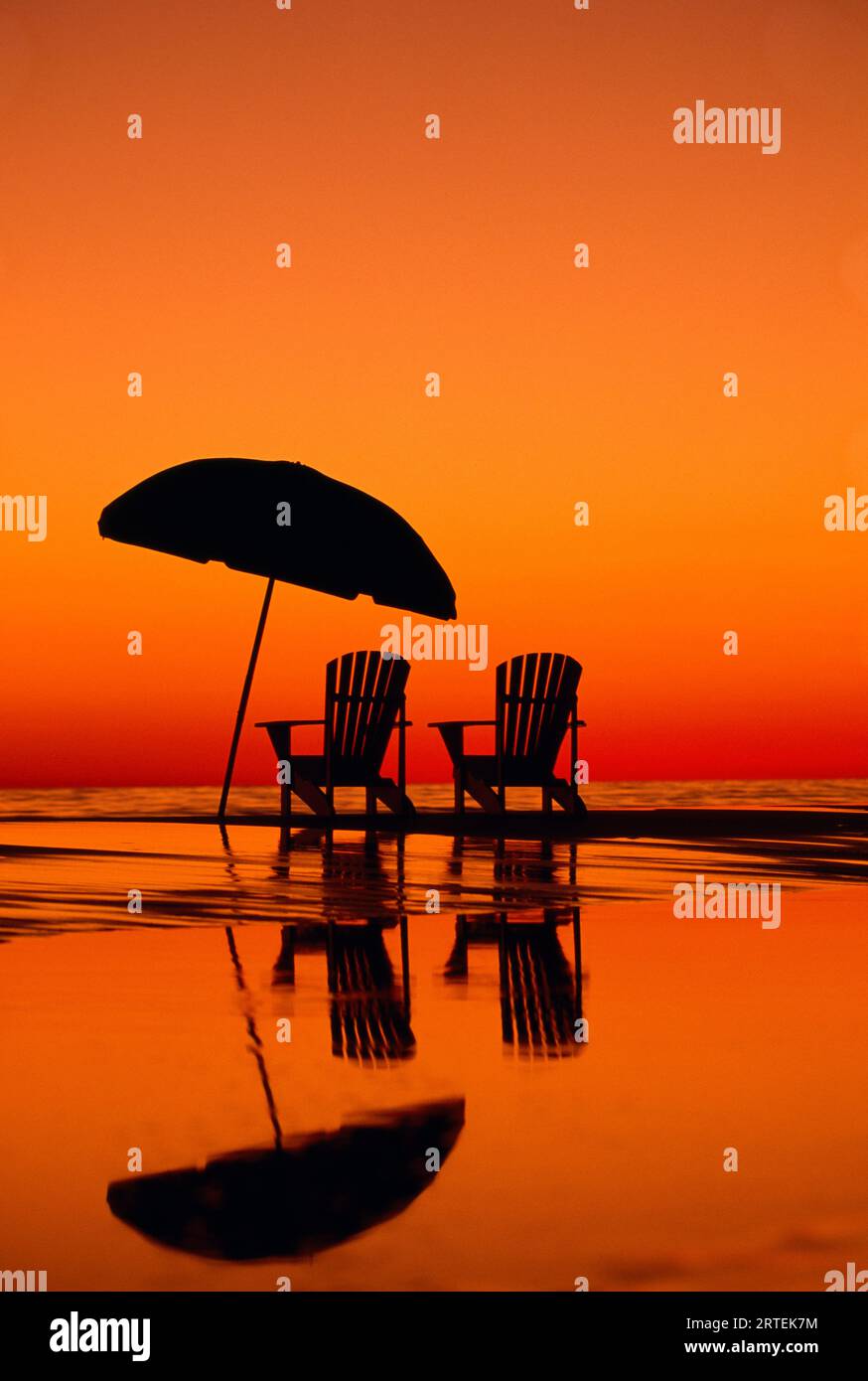 Spettacolare tramonto con due sedie e un ombrellone sulla spiaggia; Seaside, Florida, Stati Uniti d'America Foto Stock