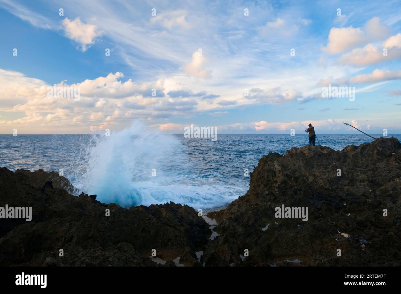 Le onde si infrangono contro la costa vicino al faro Folly mentre un pescatore si trova sulla costa rocciosa; Port Antonio, Giamaica Foto Stock