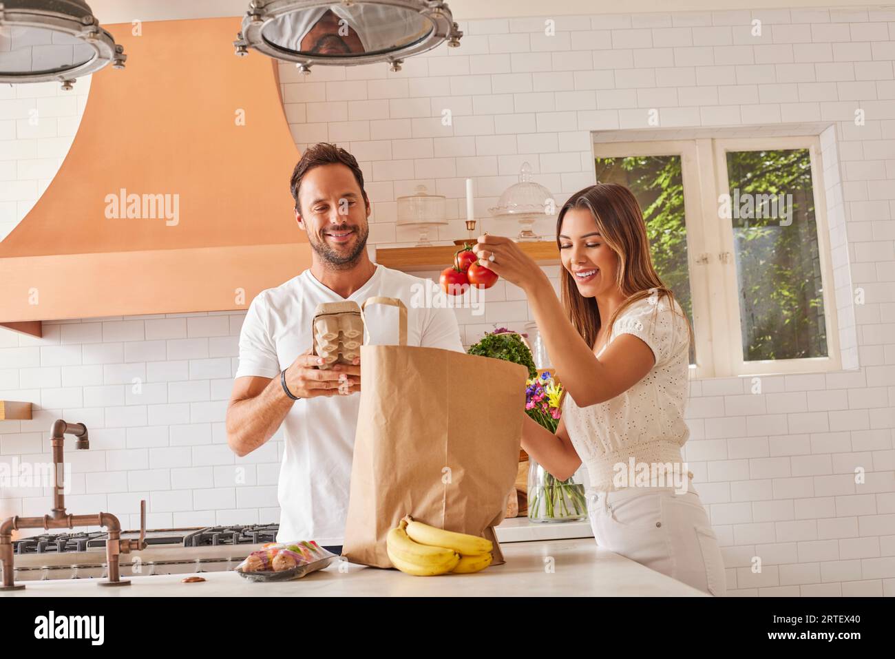 Coppia sorridente con sacchetto di carta e alimentari in cucina Foto Stock