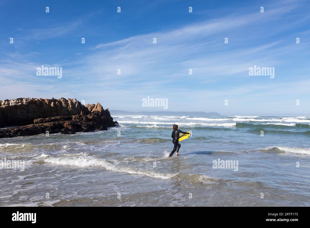 Sudafrica, Hermanus, Boy (10-11) entra nell'Oceano Atlantico con la tavola da corpo a Kammabaai Beach Foto Stock