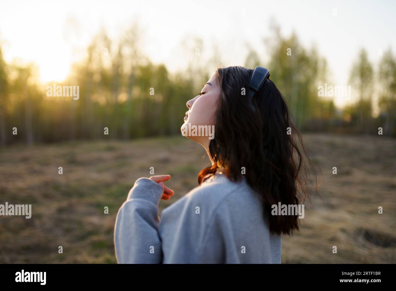 Vista laterale della donna che ascolta musica nel prato al tramonto Foto Stock