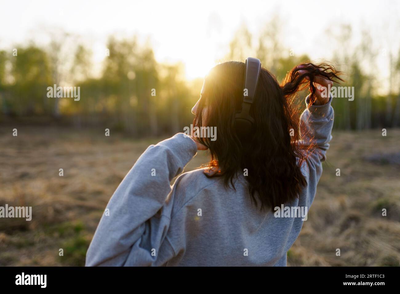 Vista posteriore di una donna che ascolta musica nel prato al tramonto Foto Stock