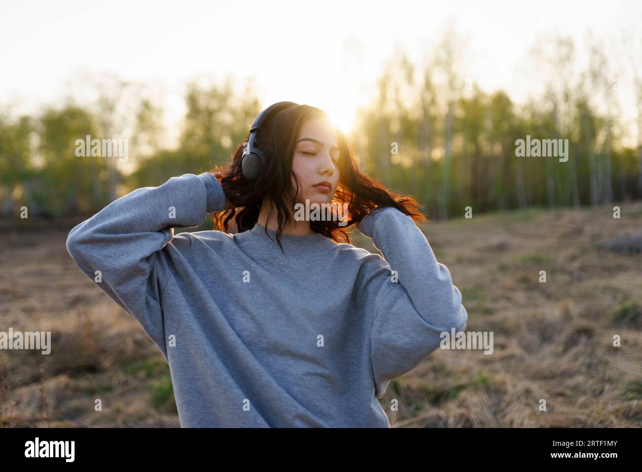 Ritratto di una donna che ascolta musica a occhi chiusi nel prato al tramonto Foto Stock