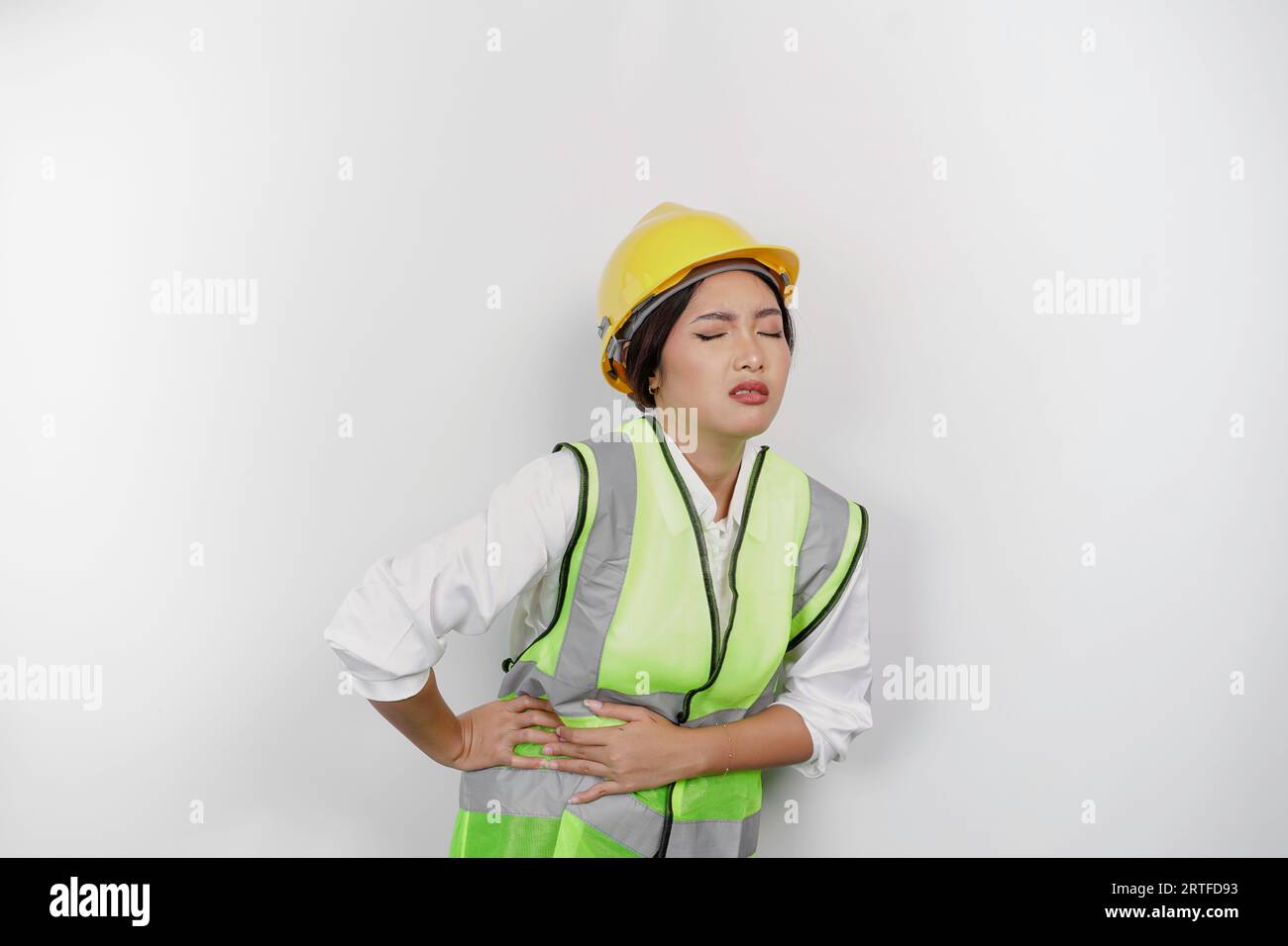 Lavoratrice asiatica che indossa un casco di sicurezza e un giubbotto tenere la mano sullo stomaco soffre di dolore sfondo bianco isolato. Concetto del giorno del lavoro. Foto Stock