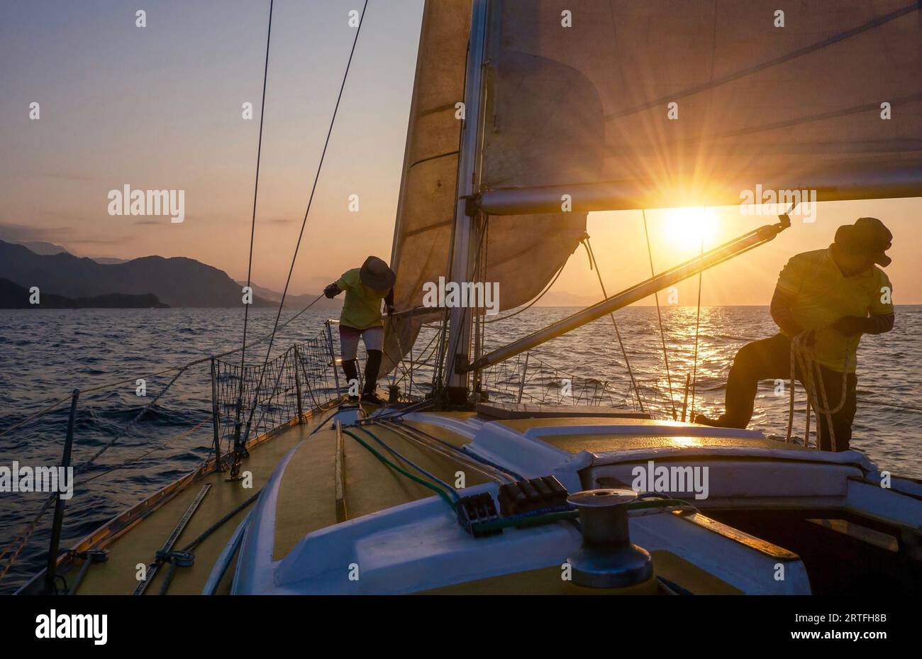 Puerto galera, Filippine - 21 marzo 2023. Una piccola barca a vela ricreativa al tramonto, con due membri dell'equipaggio di sesso maschile che effettuano cambi di vela. Foto Stock