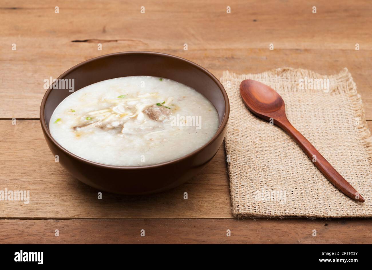 Tradizionale farinata cinese di riso con porridge in una ciotola marrone con cucchiaio di legno su un tavolo di legno Foto Stock
