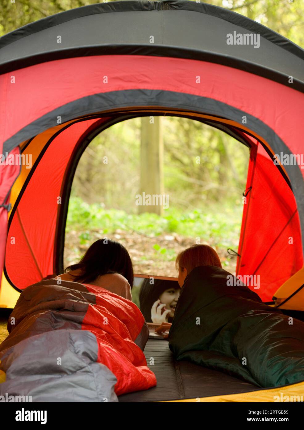 Vista posteriore di due ragazze adolescente giacente in una tenda guardando una foto su un computer portatile Foto Stock