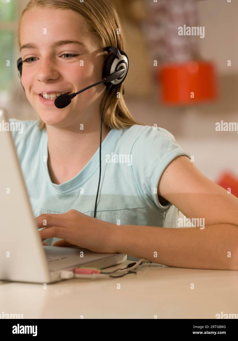 Sorridente bambina indossa le cuffie e microfono seduto alla scrivania digitando su un computer portatile Foto Stock