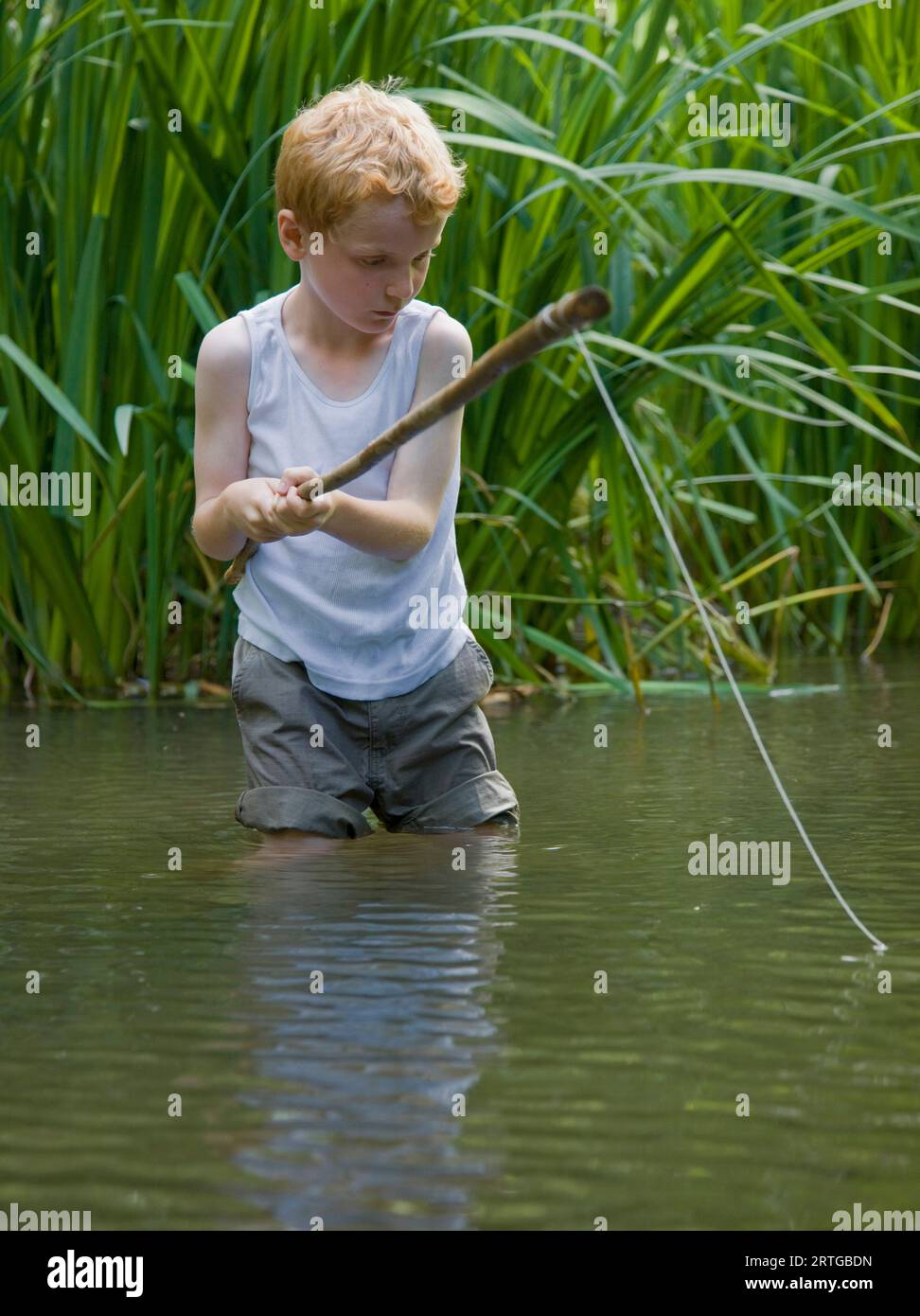 Giovane ragazzo di pesca in un fiume con le sue gambe in acqua Foto Stock