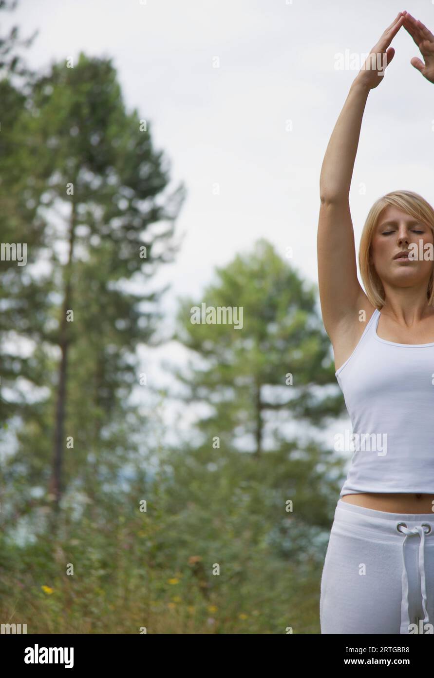 Giovane donna fare yoga in piedi in una foresta di mani alzate pongono Foto Stock