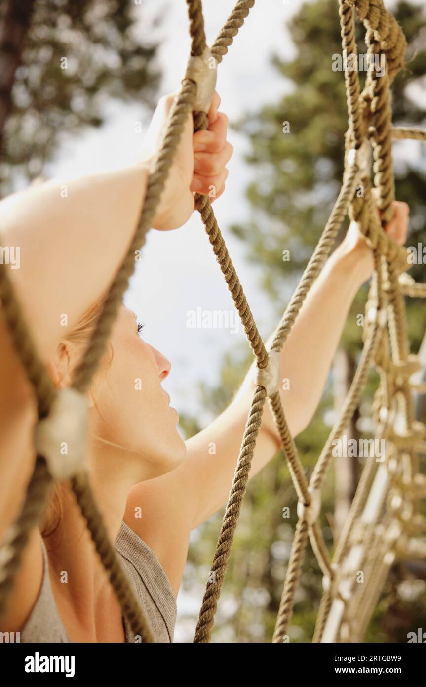 Giovane donna a ostacolo corso arrampicata un cargo net Foto Stock