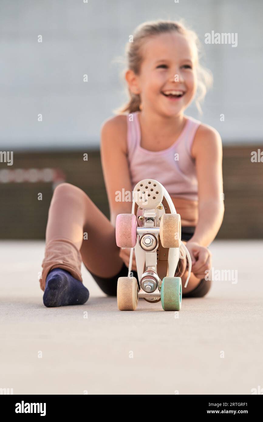 Al piano terra c'è un adorabile bambino positivo in abbigliamento sportivo e pattino a rotelle con ruote colorate sedute su un parco giochi in asfalto in città e dall'aspetto accattivante Foto Stock