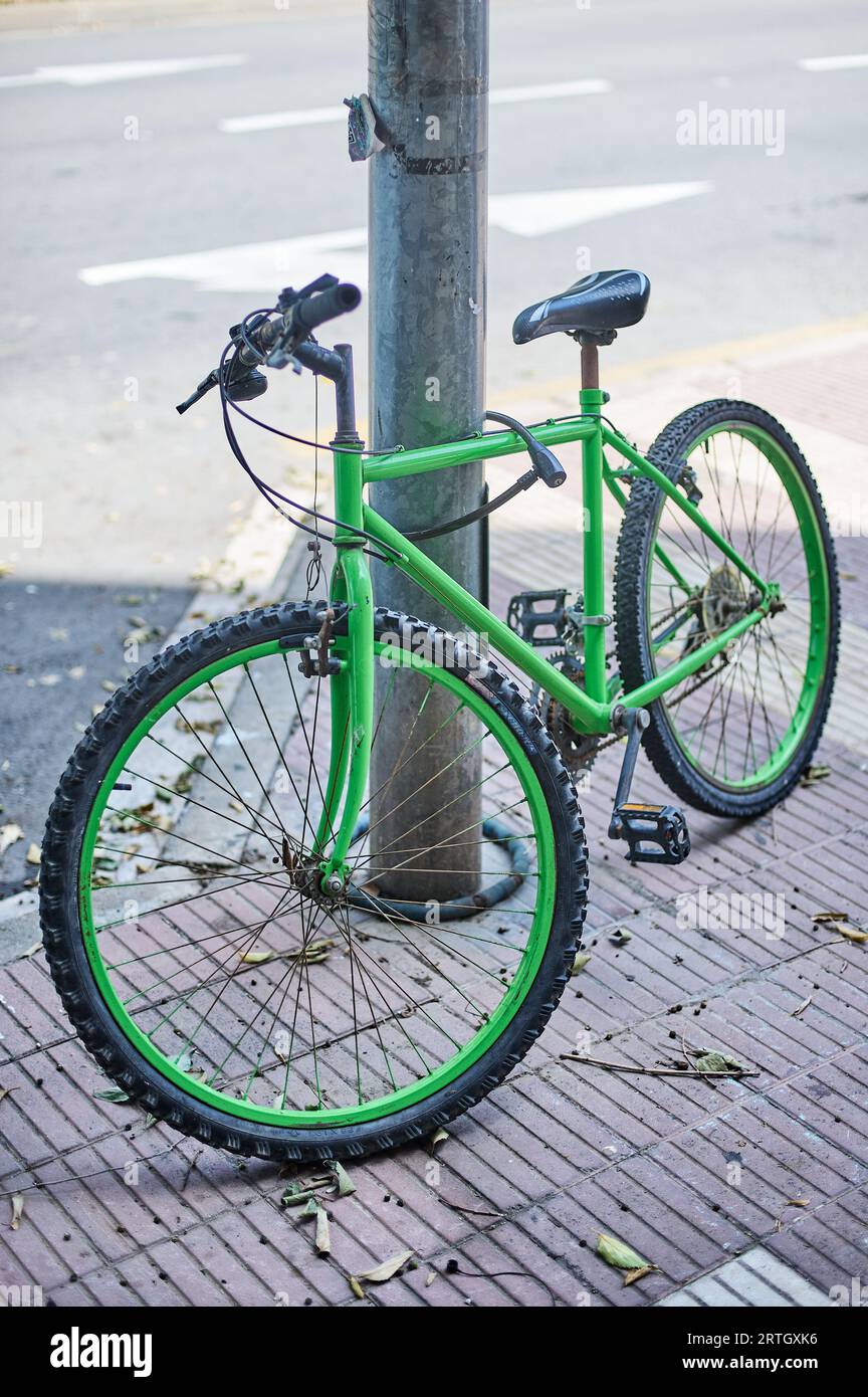 Bicicletta verde legata con un lucchetto a un lampione, nel concetto di insicurezza dei cittadini. Foto Stock
