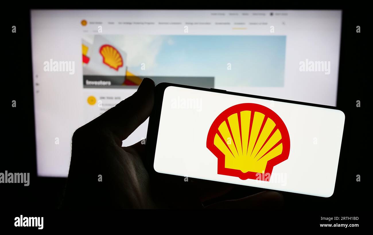 Persona in possesso di un cellulare con il logo della società britannica di petrolio e gas Shell plc sullo schermo di fronte alla pagina Web aziendale. Concentrarsi sul display del telefono. Foto Stock