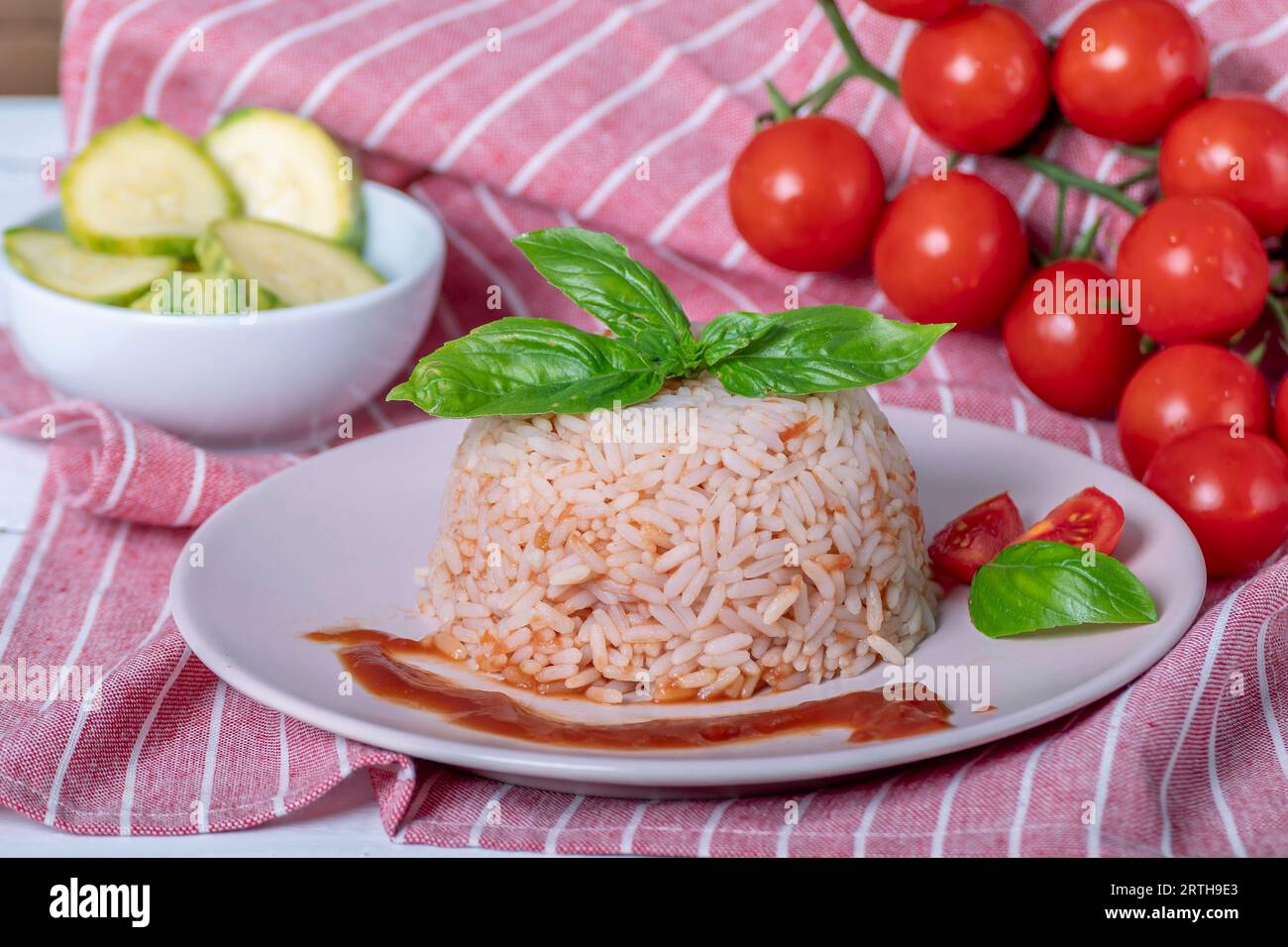 Piatto con cupola di riso al pomodoro, pomodori ciliegini rossi, foglie di basilico e zucchine tagliate a mole Foto Stock