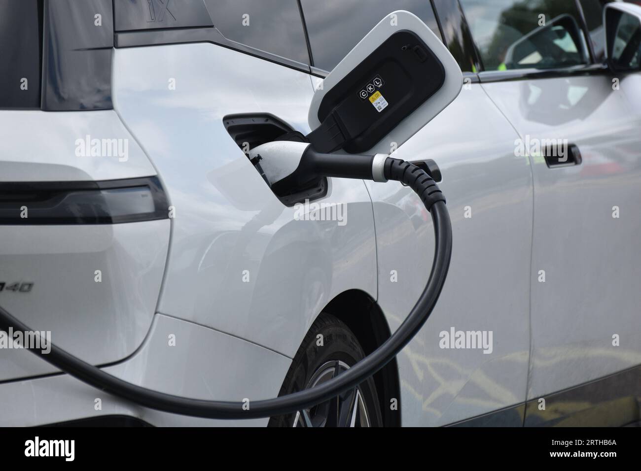 Ricarica di un veicolo elettrico bianco o di un veicolo elettrico presso una stazione di servizio su un percorso principale nel sud-ovest dell'Inghilterra Foto Stock