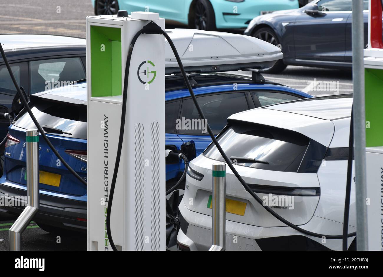 Ricarica di un veicolo elettrico bianco o di un veicolo elettrico presso una stazione di servizio su un percorso principale nel sud-ovest dell'Inghilterra Foto Stock