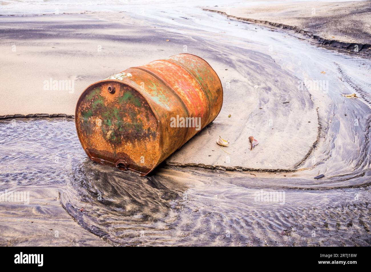 L'olio per fusti arrugginito su una spiaggia di colore parzialmente nero illustra l'inquinamento ambientale causato dalle fuoriuscite di petrolio Foto Stock