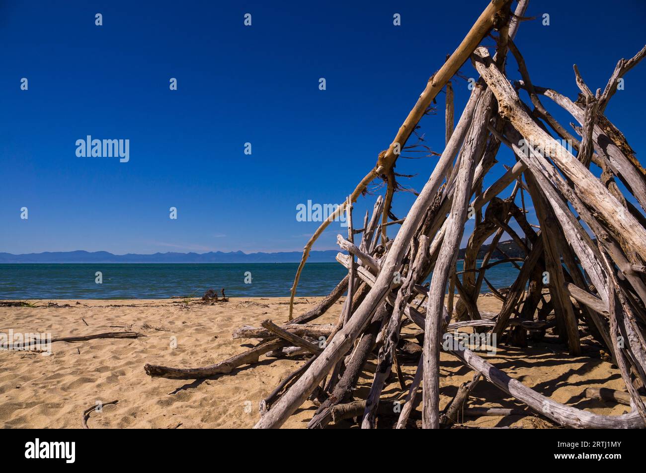 Abel Tasman NP, NUOVA ZELANDA nel febbraio 2016: Una tenda fatta di buchi si erge su una spiaggia vuota. Il cielo è blu e il sole splende Foto Stock