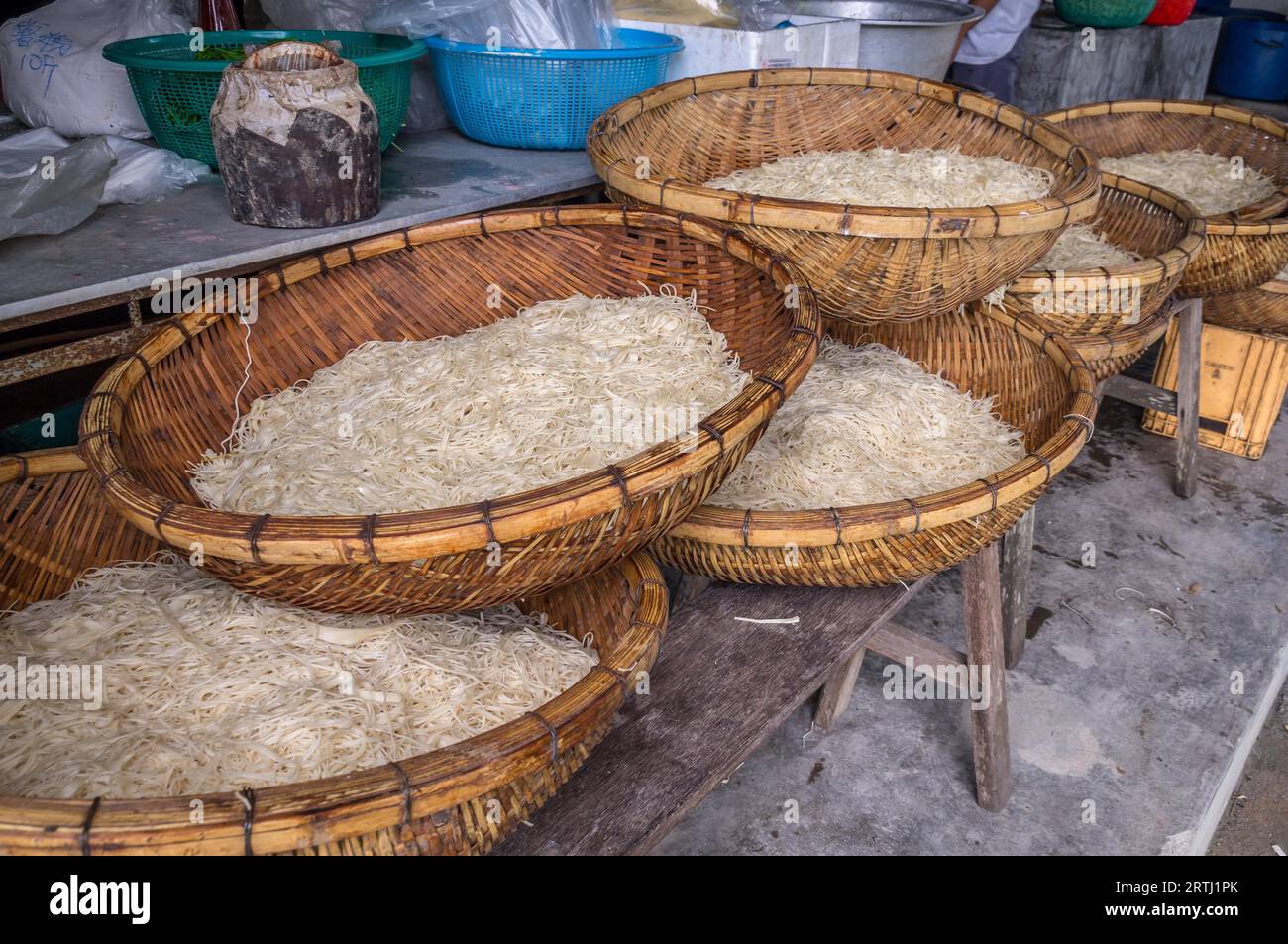 Tagliatelle di gelatina essiccate asiatiche, cibo in cesti di legno su panca di legno in una cucina rurale Foto Stock