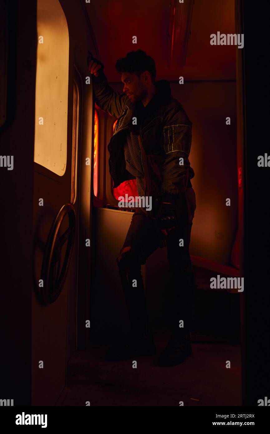 uomo con la pistola che guarda attraverso la finestra di una carrozza abbandonata in una metropolitana post-disastro con luce rossa Foto Stock