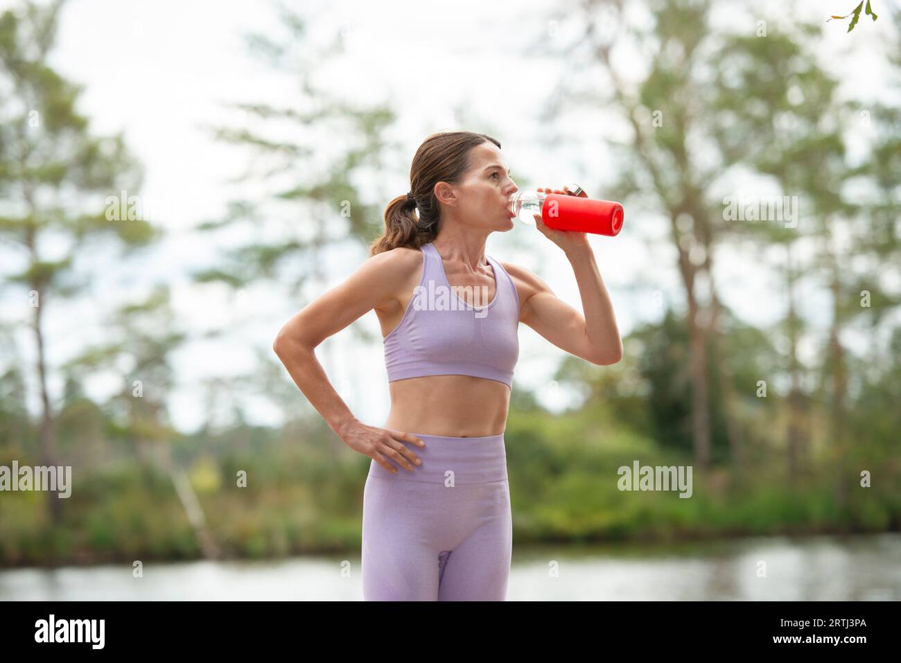 Donna sportiva che beve acqua da una bottiglia di vetro dopo l'esercizio, parte della serie. Foto Stock