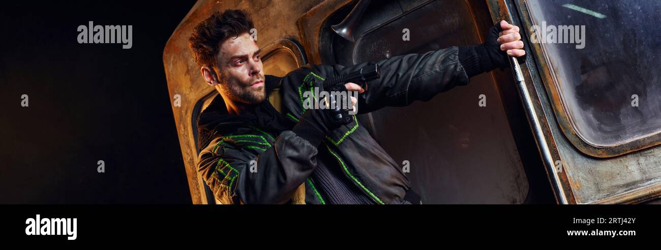 uomo incasinato che mira con la pistola nell'oscurità della metropolitana post-disastro, pericolo e sopravvivenza, striscione Foto Stock