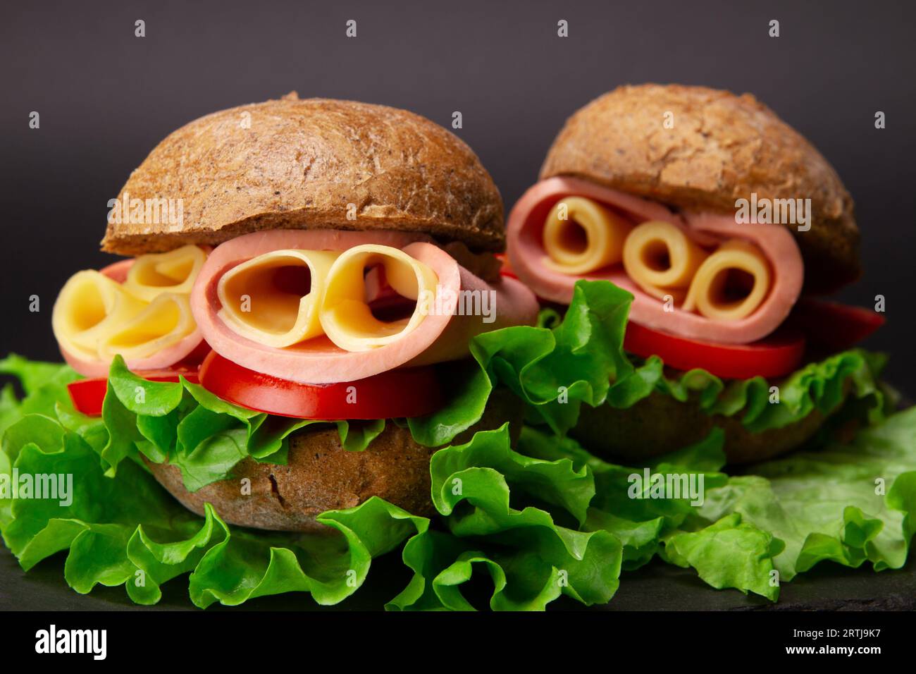 Delizioso sandwich su sfondo grigio con prosciutto, pomodori, fette di formaggio e lattuga fresca. Primo piano Foto Stock